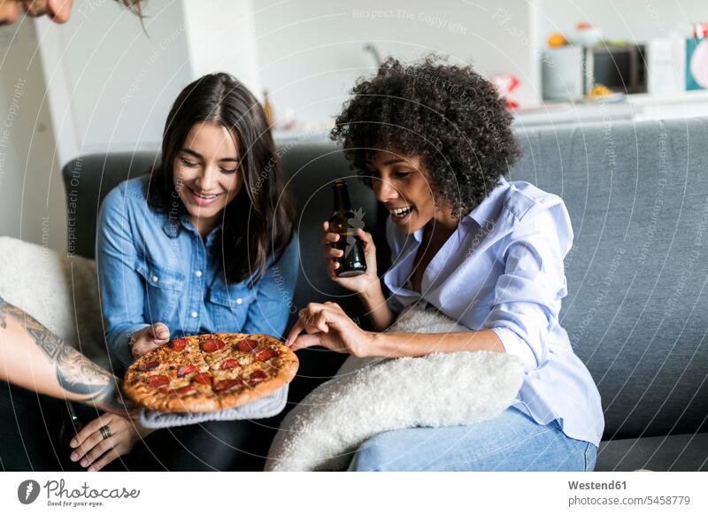 Tätowierter Mann bietet Pizza für Freunde auf der Couch sitzend Männer männlich Pizzen sitzt Sofa Couches Liege Sofas anbieten tätowiert Erwachsener erwachsen
