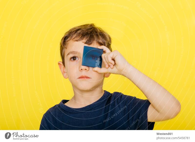 Nahaufnahme eines niedlichen Jungen, der blaues Acrylglas vor gelbem Hintergrund hält Farbaufnahme Farbe Farbfoto Farbphoto farbiger Hintergrund