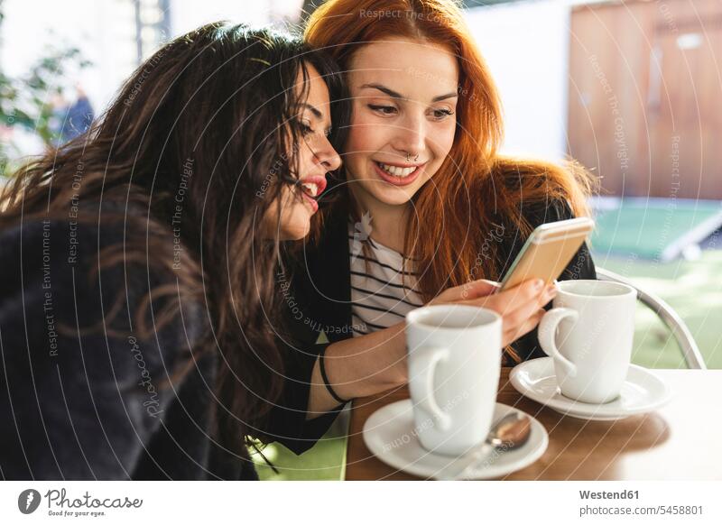Zwei Frauen schauen auf Handy am Bürgersteig Cafe Straßencafe Straßencafes Strassencafe Strassencafes Nasenpiercing Nasenpiercings weiblich Smartphone iPhone