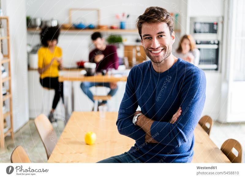 Porträt von lächelnden Mann am Esstisch zu Hause mit Freunden im Hintergrund Kameradschaft Hochschueler Hochschüler Studenten Studierende Studierender Tische
