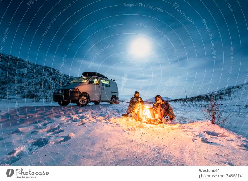 Camper am Lagerfeuer in der Winterlandschaft in der Polarnacht, Kilpisjaervi, Enontekioe, Finnland Freunde Kameradschaft Touristen sitzend sitzt nachts