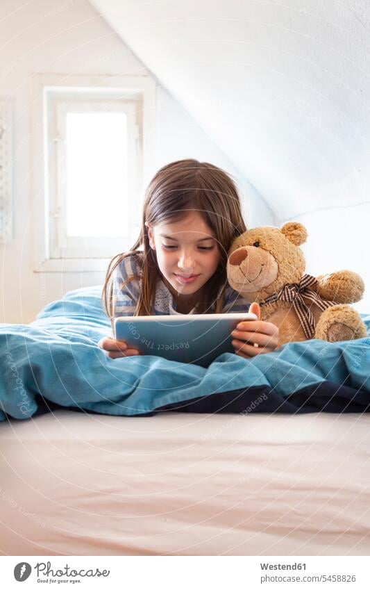 Porträt eines lächelnden Mädchens mit Teddybär auf dem Bett liegend mit digitalem Tablett Betten Teddies Teddybaer Teddybaeren Teddybären Medium entspannen