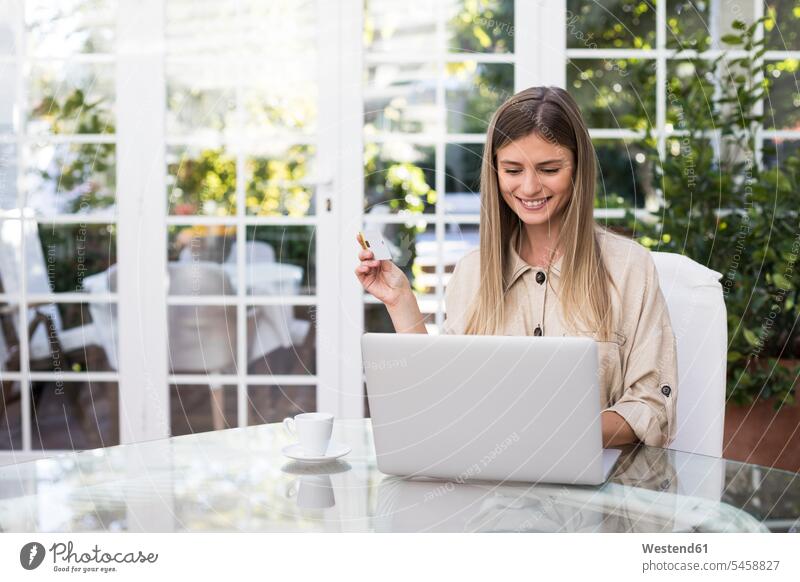 Glückliche junge Frau, die eine Kreditkarte in der Hand hält, während sie einen Laptop am Tisch im Café benutzt Farbaufnahme Farbe Farbfoto Farbphoto