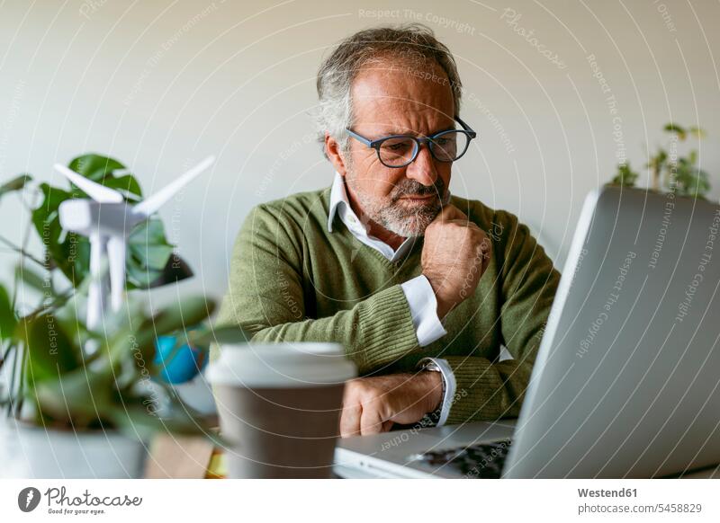 Brillenträger mit Laptop, während er zu Hause am Tisch sitzt Farbaufnahme Farbe Farbfoto Farbphoto Innenaufnahme Innenaufnahmen innen drinnen Tag