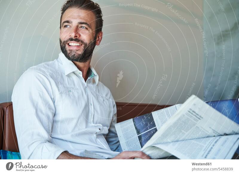 Porträt eines glücklichen Geschäftsmannes mit weißem Hemd, der mit Zeitung auf der Couch sitzt geschäftlich Geschäftsleben Geschäftswelt Geschäftsperson