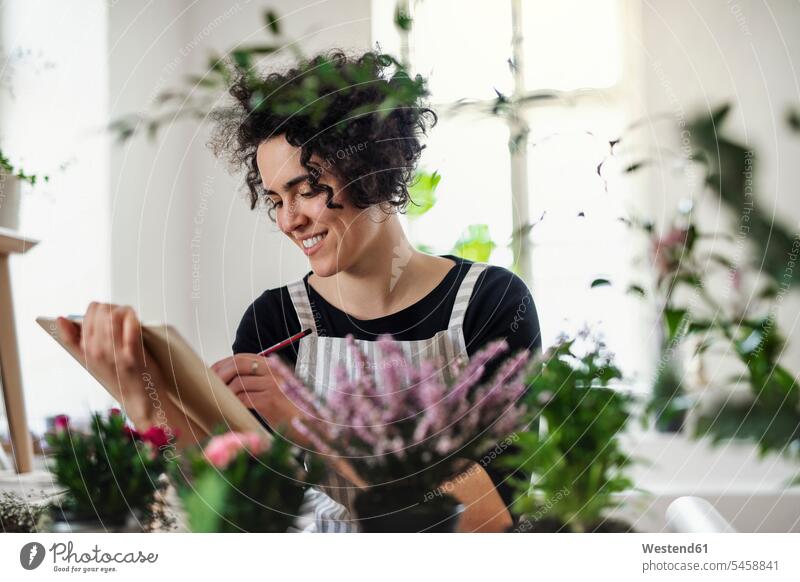 Lächelnde junge Frau mit Klemmbrett in einem kleinen Laden mit Pflanzen Job Berufe Berufstätigkeit Beschäftigung Jobs Leute Menschen People Person Personen