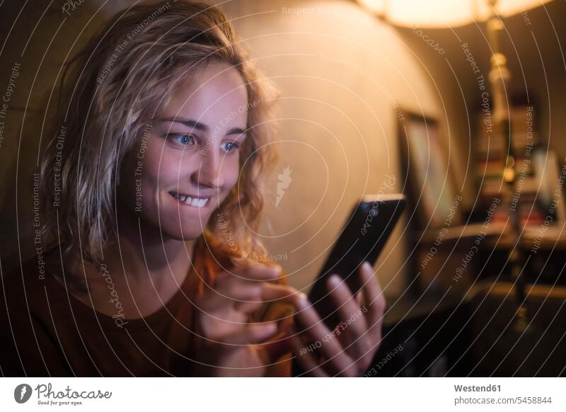 Porträt einer jungen Frau, die zu Hause ein Smartphone benutzt Informationen Telekommunikation Handies Handys Mobiltelefon Mobiltelefone Lektüre abends daheim
