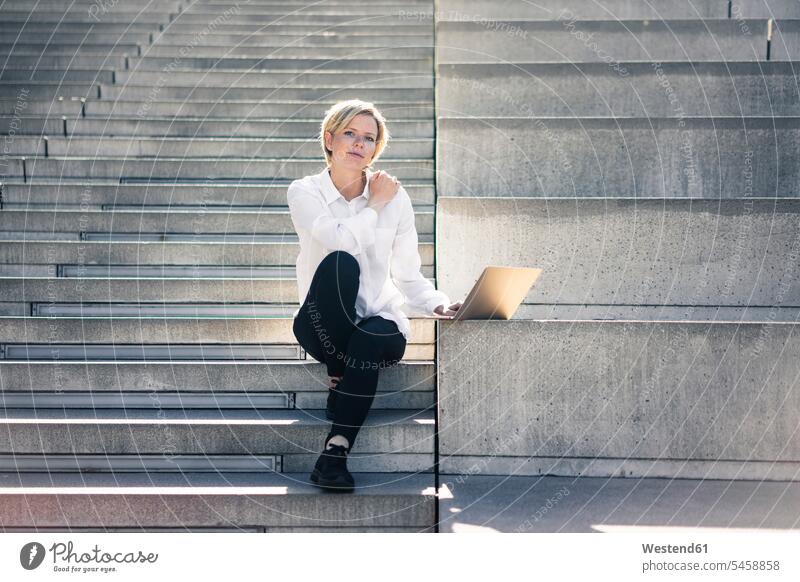 Junge Geschäftsfrau sitzt auf einer Treppe und benutzt einen Laptop Treppenaufgang Laptop benutzen Laptop benützen Karriere sitzen sitzend Notebook Laptops