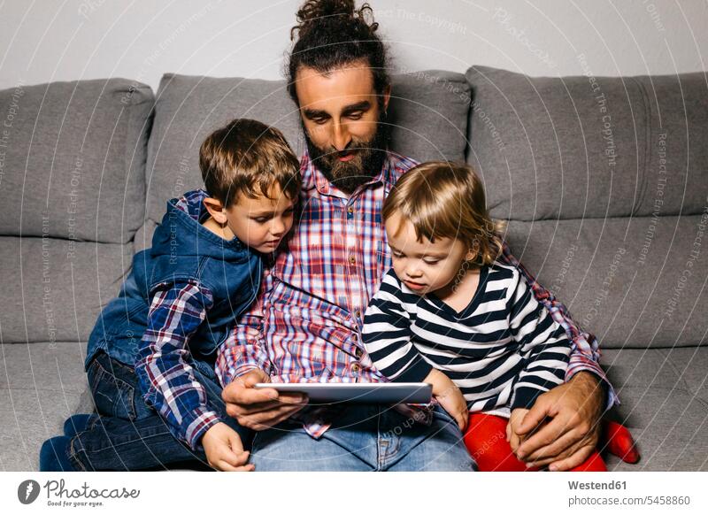 Vater sitzt mit seinen Kindern auf der Couch und schaut Filme auf einem digitalen Tablet Väter Papa Vati Familienvater Papi Tablet Computer Tablet-PC Tablet PC