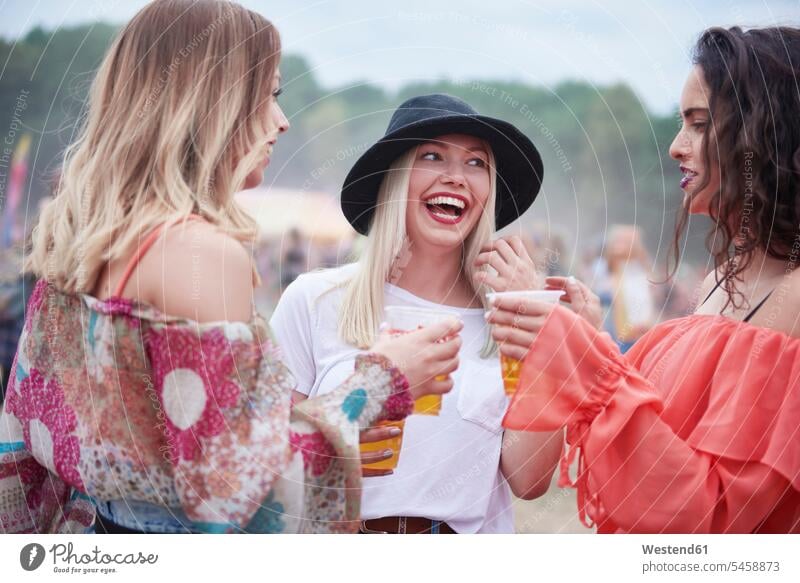 Freunde trinken Saft und sitzen während des Musikfestivals auf der Wiese Frau weiblich Frauen Festival Festivals Festspiele Freundinnen fröhlich Fröhlichkeit
