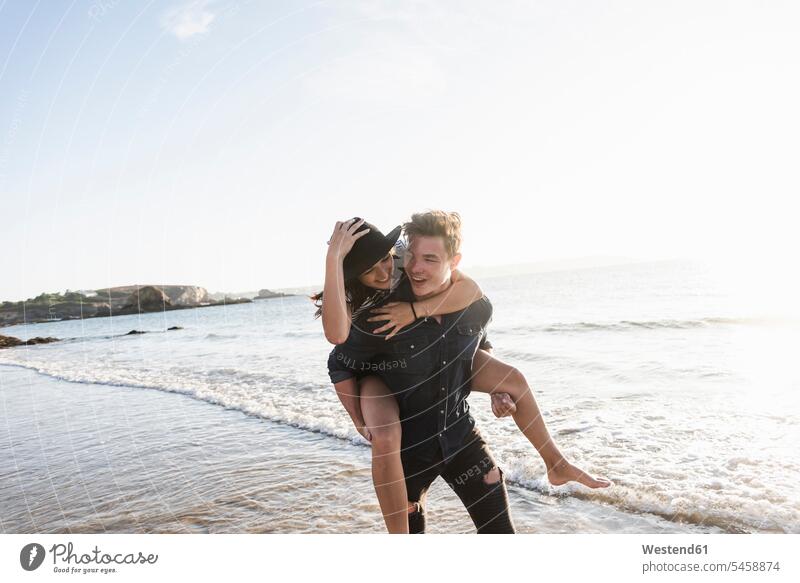 Frankreich, Bretagne, glücklicher junger Mann trägt Freundin huckepack am Strand Huckepack Paar Pärchen Paare Partnerschaft tragen transportieren Beach Straende