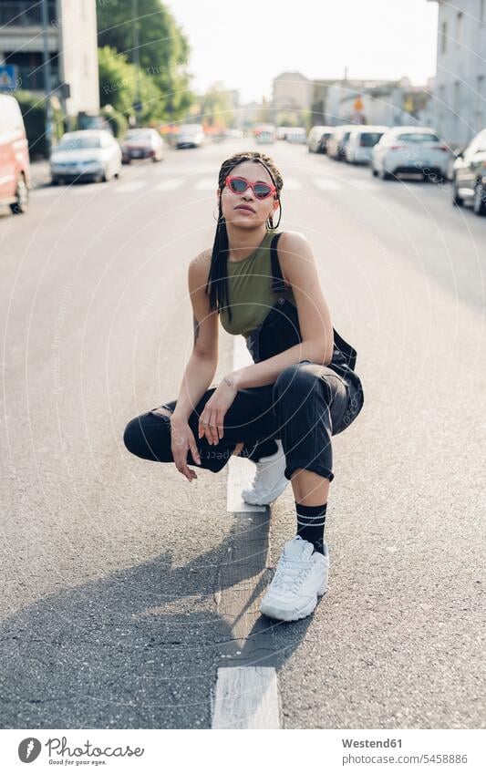 Porträt einer selbstbewussten, stilvollen jungen Frau, die auf der Straße in der Stadt kauert Brillen Sonnenbrillen Individuell Stil stylisch außen draußen