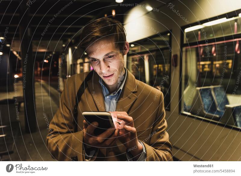 Geschäftsmann benutzt nachts sein Handy an der Straßenbahnhaltestelle Nacht Straßenbahnhaltestellen Mobiltelefon Handies Handys Mobiltelefone Businessmann