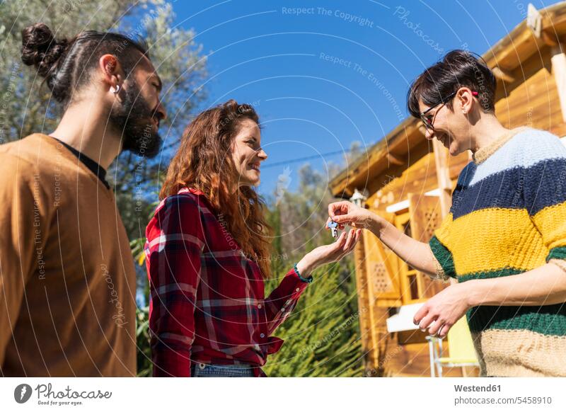 Gastgeberin empfängt junges Paar vor einer Hütte auf dem Land und übergibt den Hausschlüssel Touristen Brillen begruessen Begrüßung grüßen überreichen reden