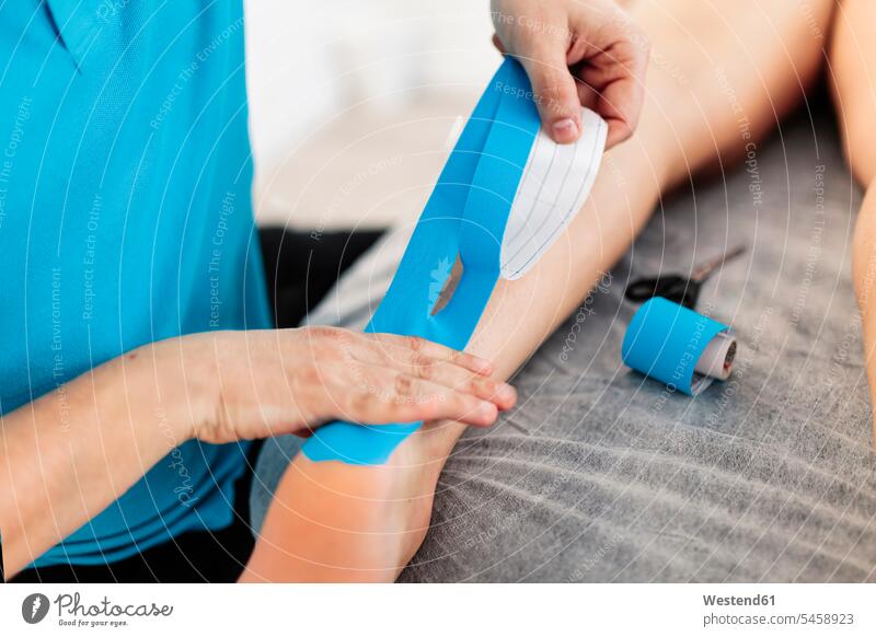 Sehbehinderter Physiotherapeut bringt in der Klinik Kinesio-Tape an der Hand des Jungen an Farbaufnahme Farbe Farbfoto Farbphoto Innenaufnahme Innenaufnahmen