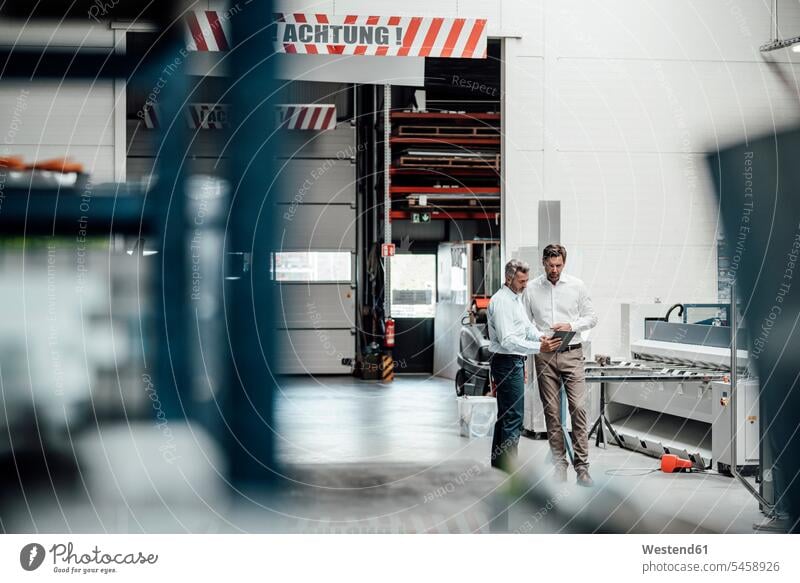 Männliche Ingenieure diskutieren über ein digitales Tablet, während sie in der Fabrik stehen Farbaufnahme Farbe Farbfoto Farbphoto Deutschland Innenaufnahme