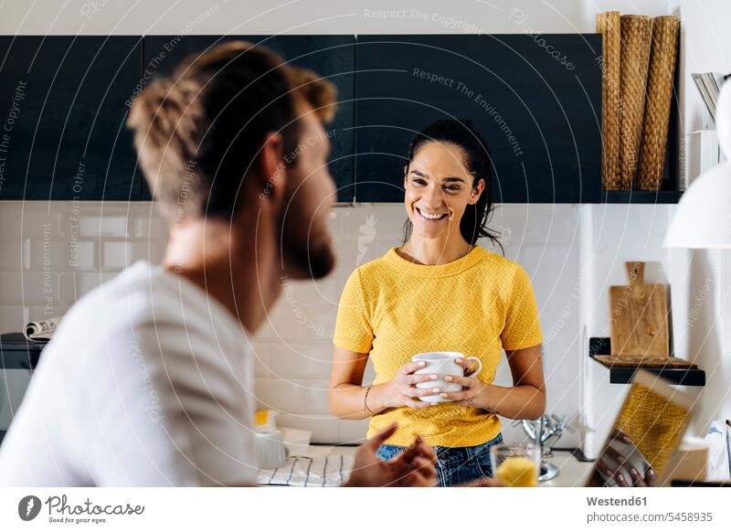 Porträt einer jungen Frau, die ihren Freund mit Laptop in der Küche anlächelt T-Shirts Rechner Laptops Notebook Notebooks früh Frühe Morgen freuen Frohsinn