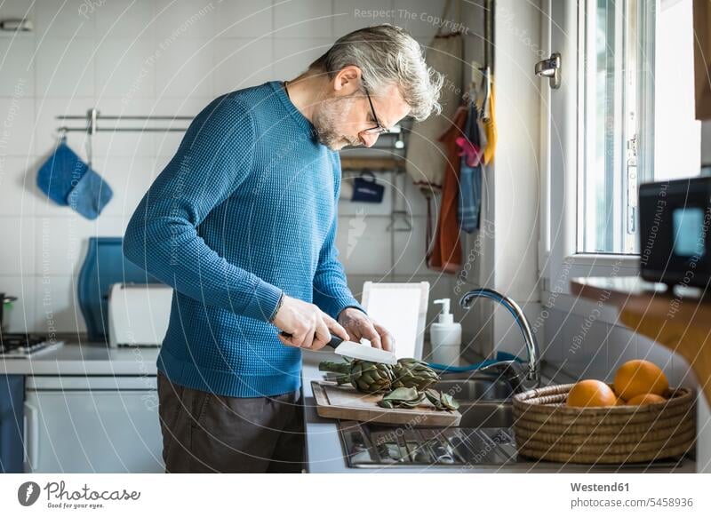 Reifer Mann bereitet in seiner Küche Artischocken zu Leute Menschen People Person Personen Alleinstehende Alleinstehender Singles Unverheiratete Unverheirateter