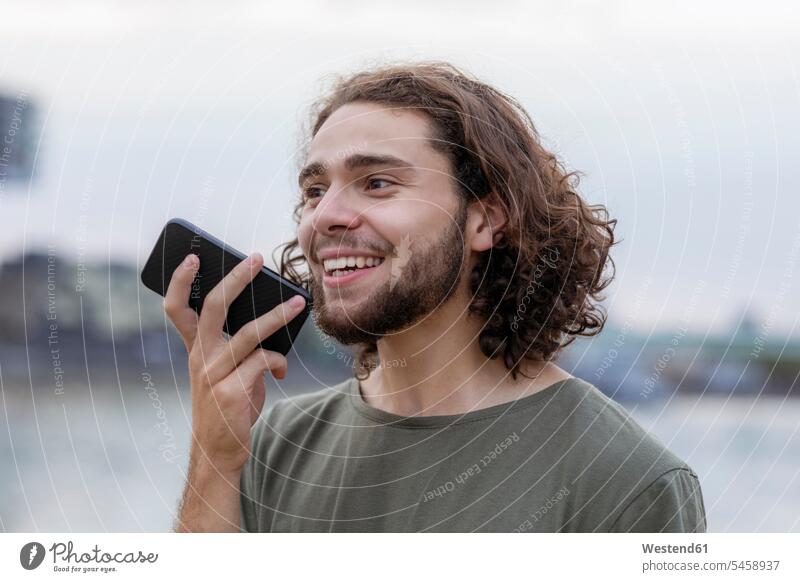 Porträt eines glücklichen jungen Mannes, der sein Smartphone im Freien benutzt iPhone Smartphones Portrait Porträts Portraits lächeln Glück glücklich sein