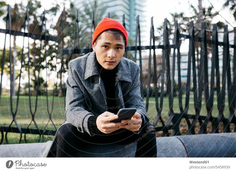 Spanien, Barcelona, Porträt eines modischen jungen Mannes mit Mobiltelefon Portrait Porträts Portraits sitzen sitzend sitzt Männer männlich Smartphone iPhone
