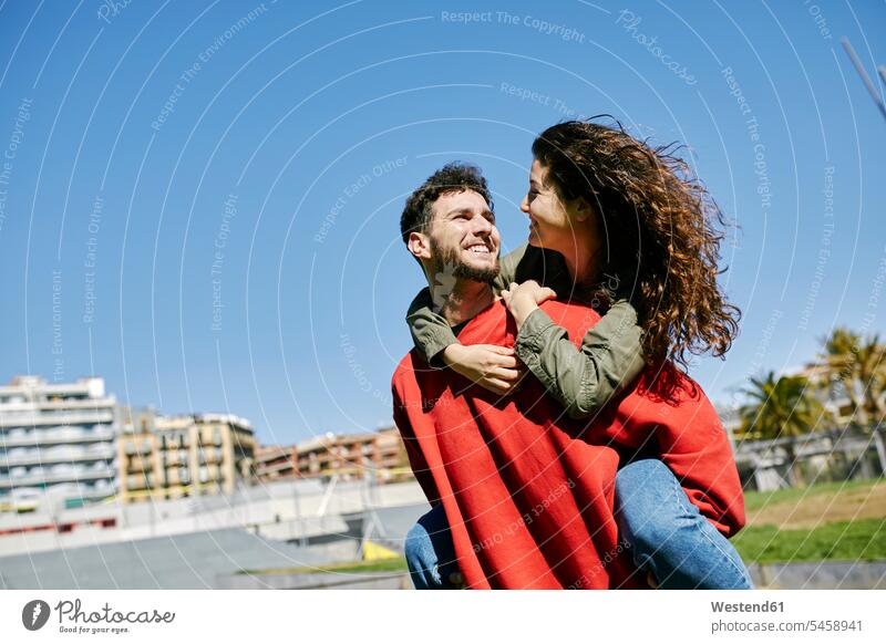 Glücklicher junger Mann nimmt seine Freundin Huckepack Paar Pärchen Paare Partnerschaft glücklich glücklich sein glücklichsein Mensch Menschen Leute People