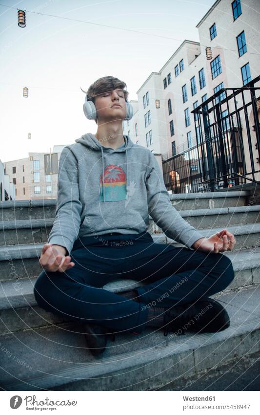 Teenager sitzt auf Stufen, meditiert in der Stadt und hört Musik Kopfhoerer entspannen relaxen hoeren sitzend Glück glücklich sein glücklichsein zufrieden Muße