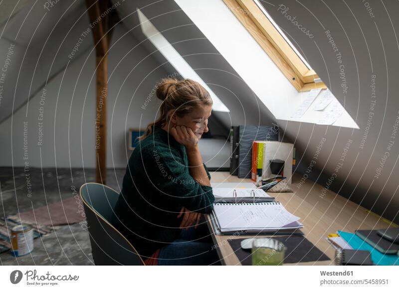 Junge Frau sitzt am Schreibtisch auf dem Dachboden und studiert einen Ordner Deutschland Erfrischungsgetränk Erfrischungsgetraenk Softdrink Wohnung wohnen