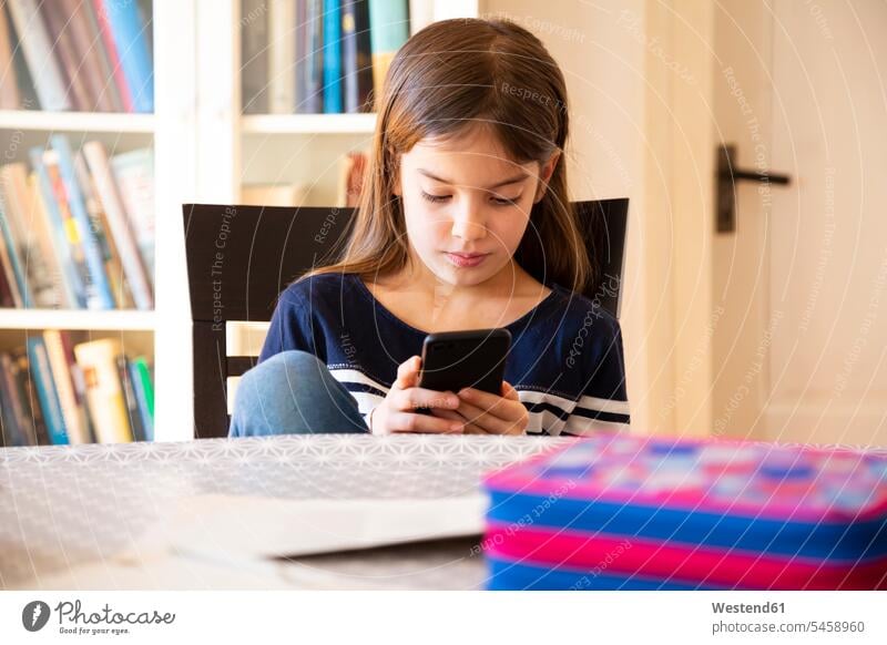 Mädchen macht Hausaufgaben mit Smartphone Ablage Regale Bücherregale Tische Handies Handys Mobiltelefon Mobiltelefone sitzend sitzt daheim zu Hause