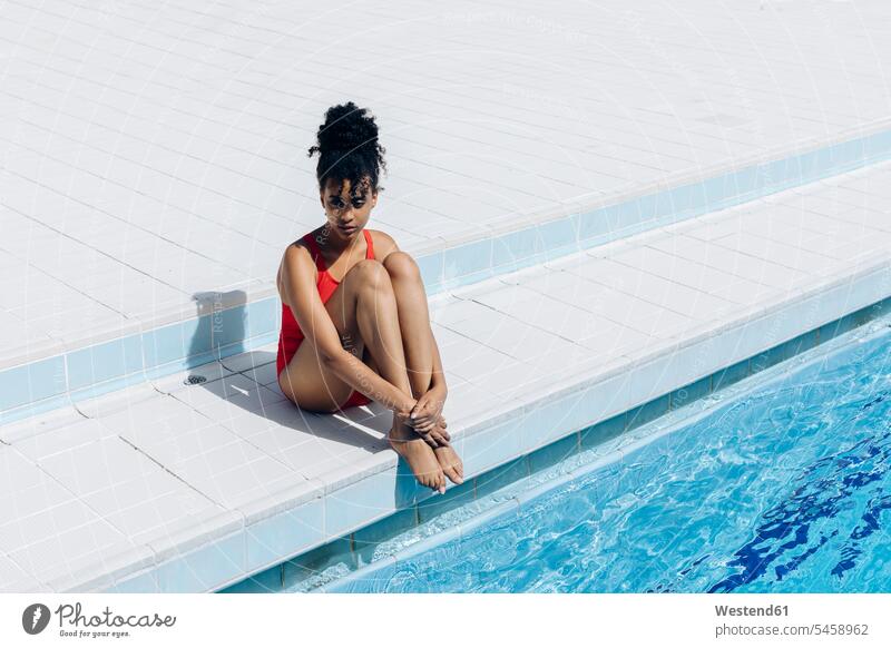 Nachdenkliche junge Frau im roten Badeanzug sitzt am Pool Fliesen Kachel Kacheln Badebekleidung Badeanzuege Badeanzüge entspannen relaxen sitzend Jahreszeiten