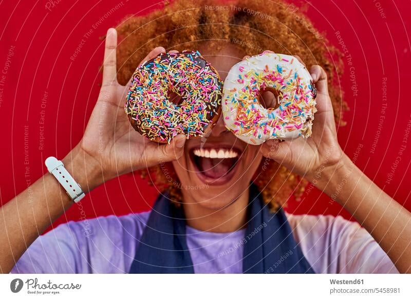 Verspielte Frau hält zwei Donuts vor ihren Augen Leute Menschen People Person Personen Afrikanisch Afrikanische Abstammung dunkelhäutig Farbige Farbiger