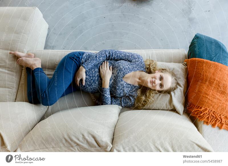 Porträt einer lächelnden schwangeren Frau, die zu Hause auf der Couch liegt liegen liegend Zuhause daheim Portrait Porträts Portraits weiblich Frauen Schwangere