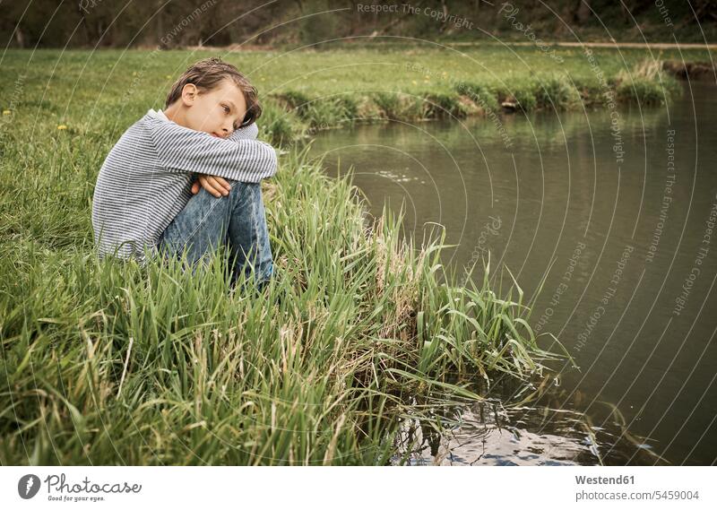 Seitenansicht eines einsamen Jungen, der am Flussufer sitzt und im Wald denkt Farbaufnahme Farbe Farbfoto Farbphoto Deutschland Außenaufnahme außen draußen