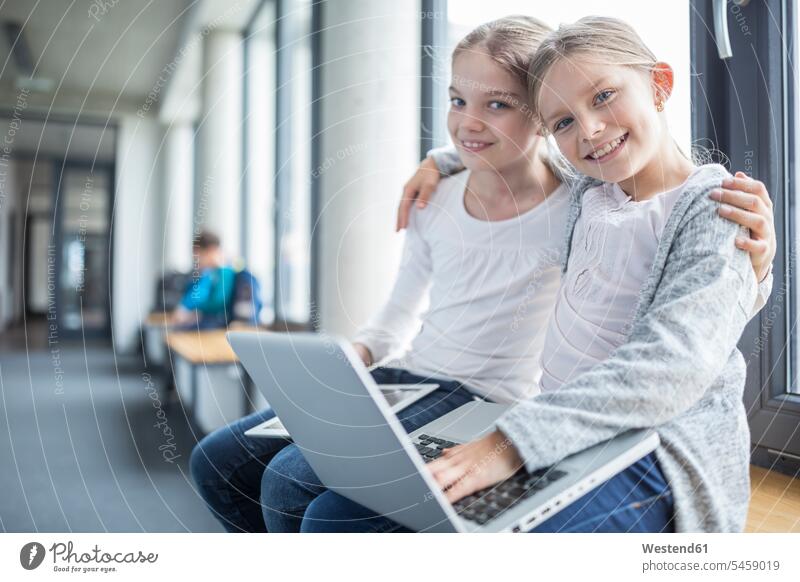 Porträt von zwei lächelnden Schulmädchen mit Laptop und Tablett in der Umarmung Korridor Flur Gang Fure Korridore Gänge Gaenge Schule Schulen Schülerin