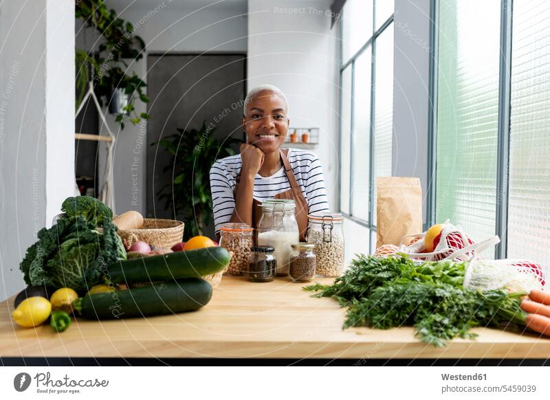 Frau mit Schürze in der Küche , Auspacken frisch gekauften Bio-Obst und Gemüse Leute Menschen People Person Personen Afrikanisch Afrikanische Abstammung