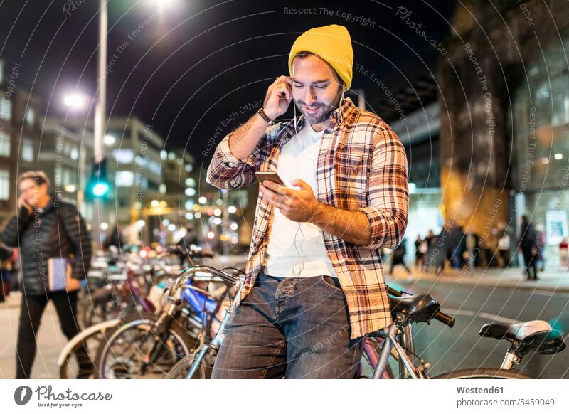 UK, London, Mann pendelt nachts in der Stadt und schaut auf sein Telefon ansehen Nacht Handy Mobiltelefon Handies Handys Mobiltelefone pendeln glücklich Glück