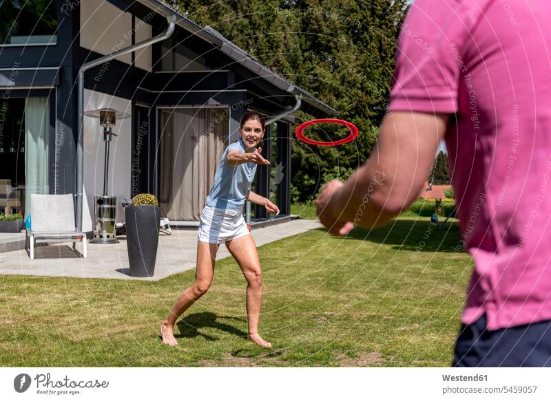 Glückliches Paar spielt mit fliegender Scheibe im Garten seines Hauses Wurfscheibe Frisbee Wurfscheiben Flugscheiben spielen Häuser Haeuser Pärchen Paare