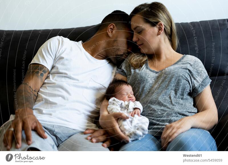 Eltern kuscheln mit neugeborenem Baby auf der Couch Wohnzimmer Wohnraum Wohnung Wohnen Wohnräume Wohnungen küssen Küsse Kuss behüten Babies Babys Säuglinge Kind