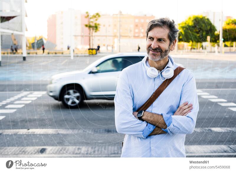 Porträt eines lächelnden reifen Mannes mit Kopfhörern, der an einer Straße steht Strassen Straßen Männer männlich Portrait Porträts Portraits stehen stehend