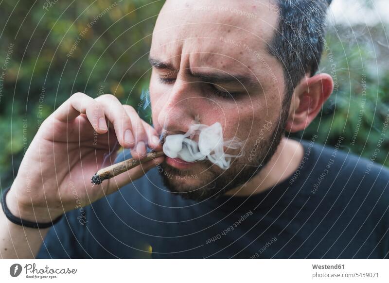 Hübscher Mann raucht Marihuana-Joint im Freien Farbaufnahme Farbe Farbfoto Farbphoto Außenaufnahme außen draußen Tag Tageslichtaufnahme Tageslichtaufnahmen