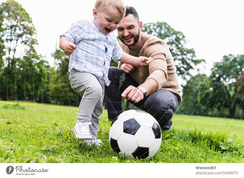 Glücklicher Vater spielt mit seinem Sohn in einem Park Fussball Söhne spielen aktiv glücklich glücklich sein glücklichsein Parkanlagen Parks Fußball Papas Väter