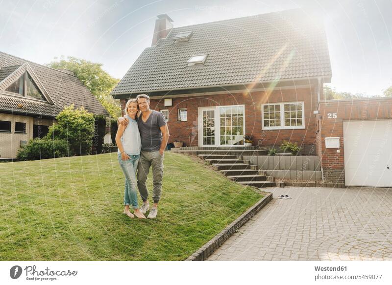 Lächelndes reifes Paar umarmt sich im Garten ihres Hauses lächeln Gärten Gaerten Pärchen Paare Partnerschaft Häuser Haeuser umarmen Umarmung Umarmungen