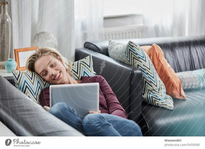 Lächelnde junge Frau mit Tablet auf der Couch liegend zu Hause liegt lächeln weiblich Frauen Sofa Couches Liege Sofas Tablet Computer Tablet-PC Tablet PC iPad