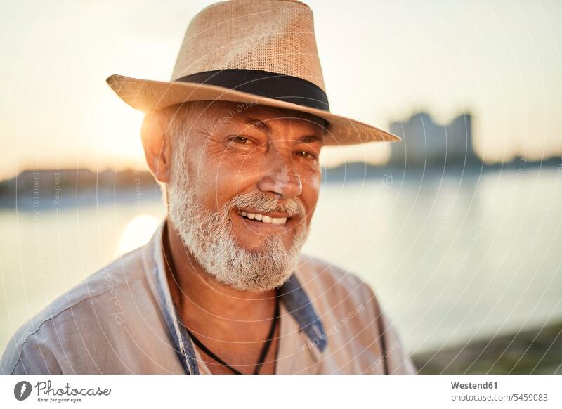 Porträt eines lächelnden älteren Mannes mit Sommerhut am Flussufer bei Sonnenuntergang Leute Menschen People Person Personen Europäisch Kaukasier kaukasisch 1