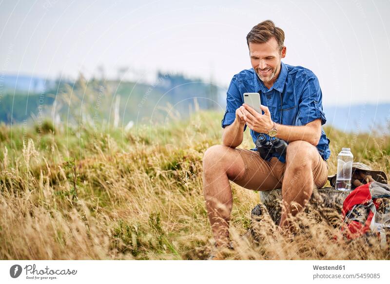 Lächelnder Mann ruht sich aus und überprüft sein Handy während einer Wanderung checken Wandertour wandern lächeln Männer männlich rasten Rast ausruhen