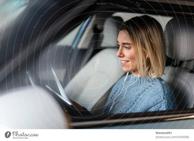 Lächelnde junge Frau mit Dokumenten, Tablett und Kopfhörern in einem Auto Papiere Unterlagen Transport Transportwesen KFZ Verkehrsmittel Automobil Autos PKW