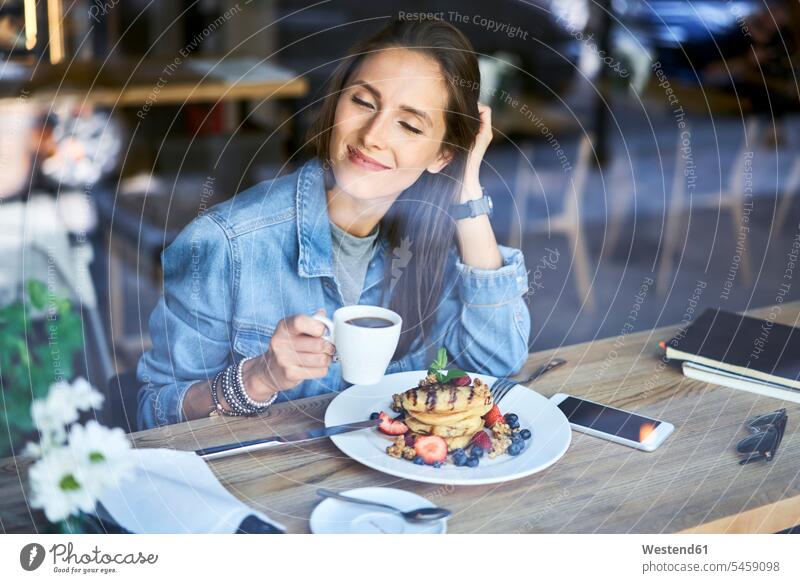 Lächelnde junge Frau, die Pfannkuchen und Kaffee im Café genießt Cafe Kaffeehaus Bistro Cafes Cafés Kaffeehäuser lächeln genießen geniessen Genuss Pancake