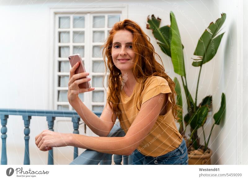 Porträt einer lächelnden rothaarigen jungen Frau mit Smartphone an der Reling lehnend T-Shirts Telekommunikation Handies Handys Mobiltelefon Mobiltelefone