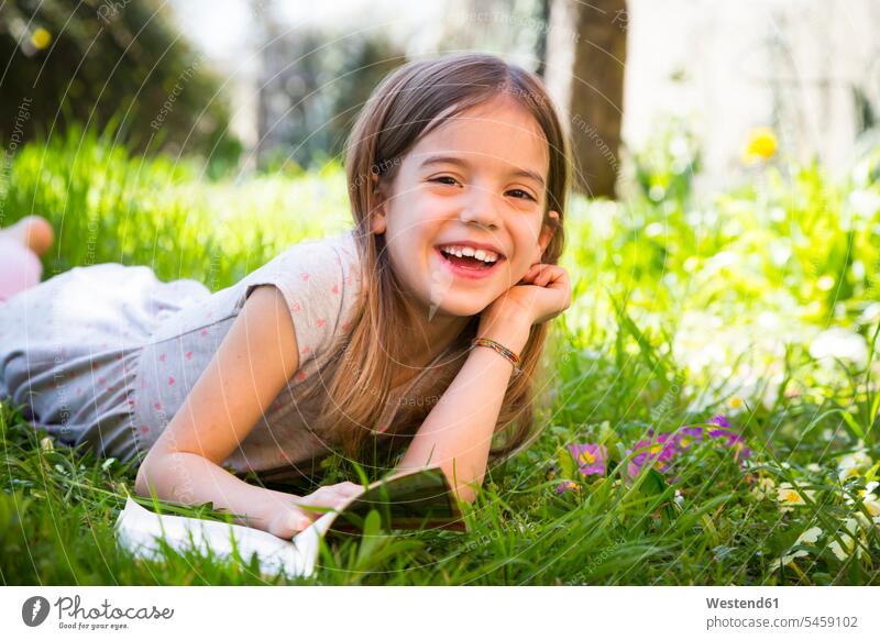 Lächelndes Mädchen liegt auf der Wiese und liest ein Buch lachen liegen lesen Freizeit lächeln positiv Emotion emotional Freude Natur Außenaufnahme Rasen