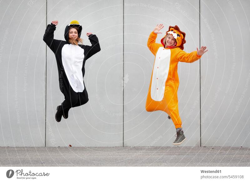 Zwei Frauen in Pinguin- und Löwenkostüm springen vor Betonmauer Loewe Loewen begeistert Enthusiasmus enthusiastisch Überschwang Überschwenglichkeit freuen