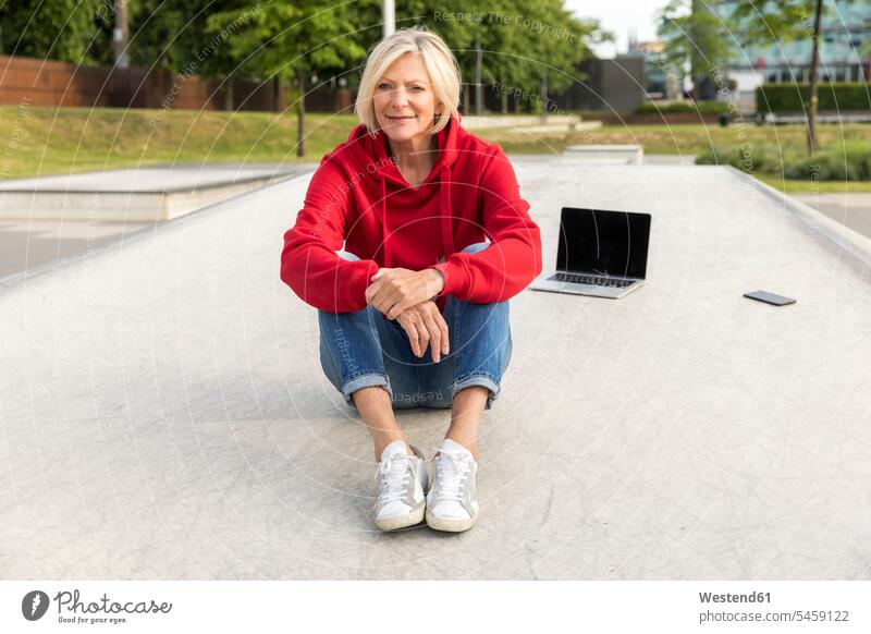 Ältere Frau mit roter Kapuze sitzt mit Laptop im Freien weiblich Frauen rotes sitzen sitzend Notebook Laptops Notebooks lächeln Zuversicht Zuversichtlich